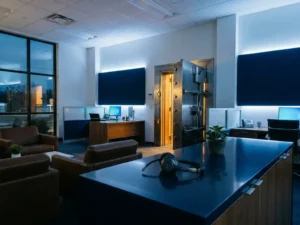 Zware kluisdeur op een kier in modern kantoor, headset op gepolijst bureau, warm goudlicht contrasteert met koel blauw sfeerli­cht.